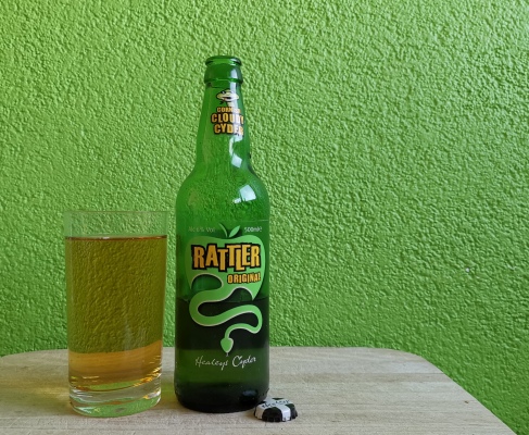 Flasche Rattler Original und ein eingeschenktes Glas mit einer leicht braunen, durchsichtigen Flüssigkeit.